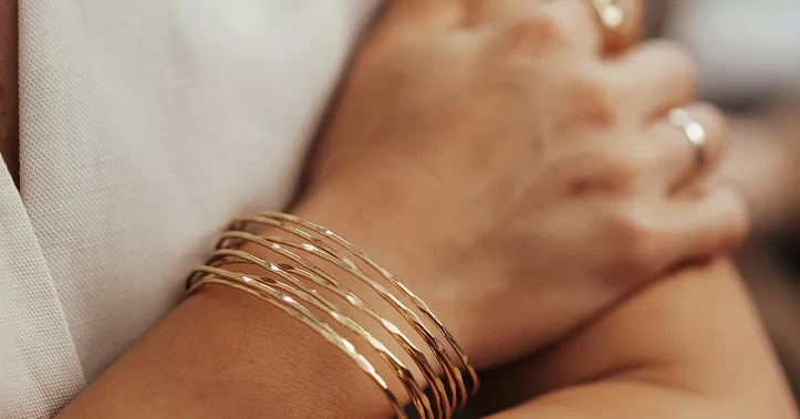 Side profile showing woman's ear with gold hoop earring featuring pearl accents, brown hair tucked behind ear in intimate beauty detail shot
