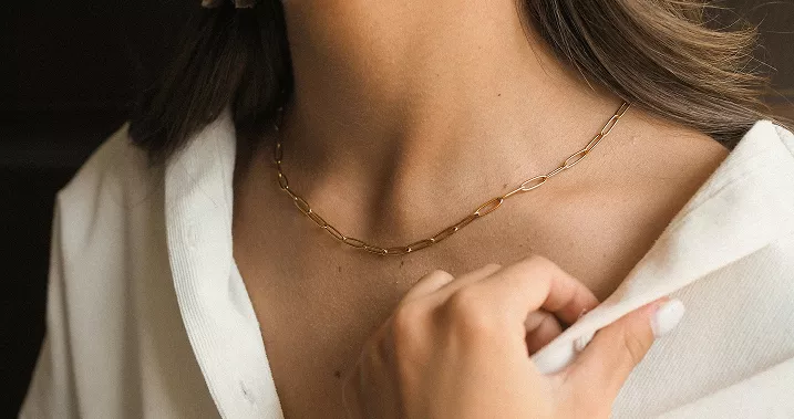 Side profile showing woman's ear with gold hoop earring featuring pearl accents, brown hair tucked behind ear in intimate beauty detail shot