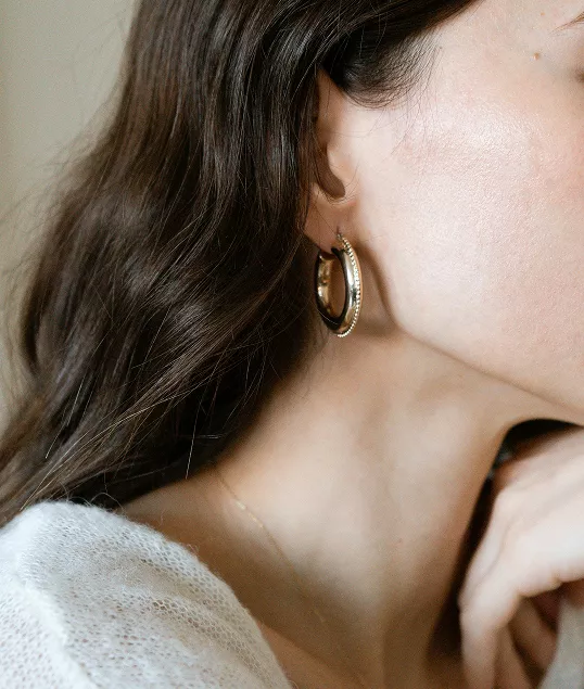 Profile view of woman wearing large gold hoop earrings with textured finish, brunette hair flowing, elegant minimalist aesthetic shown.