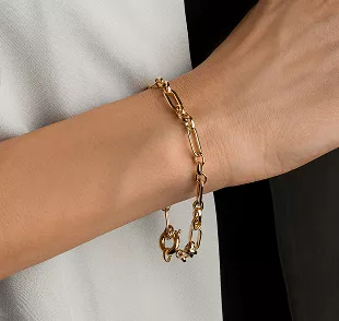 Wrist modeling chunky gold chain link bracelet against white clothing, showcasing modern minimalist jewelry with warm metallic tones.
