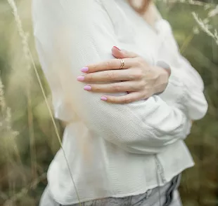 Wrist modeling chunky gold chain link bracelet against white clothing, showcasing modern minimalist jewelry with warm metallic tones.