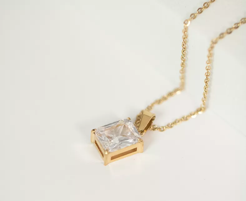 Gold necklace with emerald-cut clear crystal pendant in prong setting on delicate chain against white background in elegant product shot