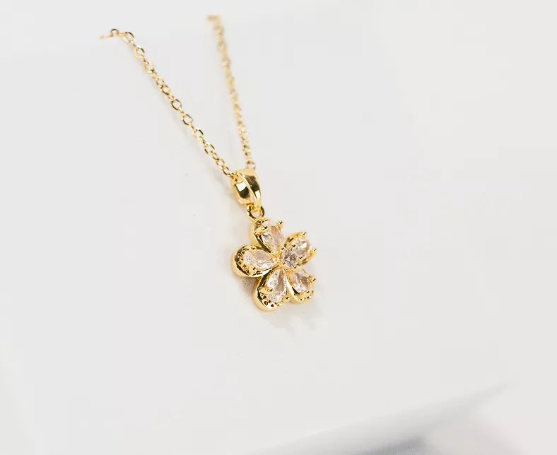 Gold flower pendant necklace with five pear-shaped clear crystal petals on fine chain displayed on white surface in detailed product view