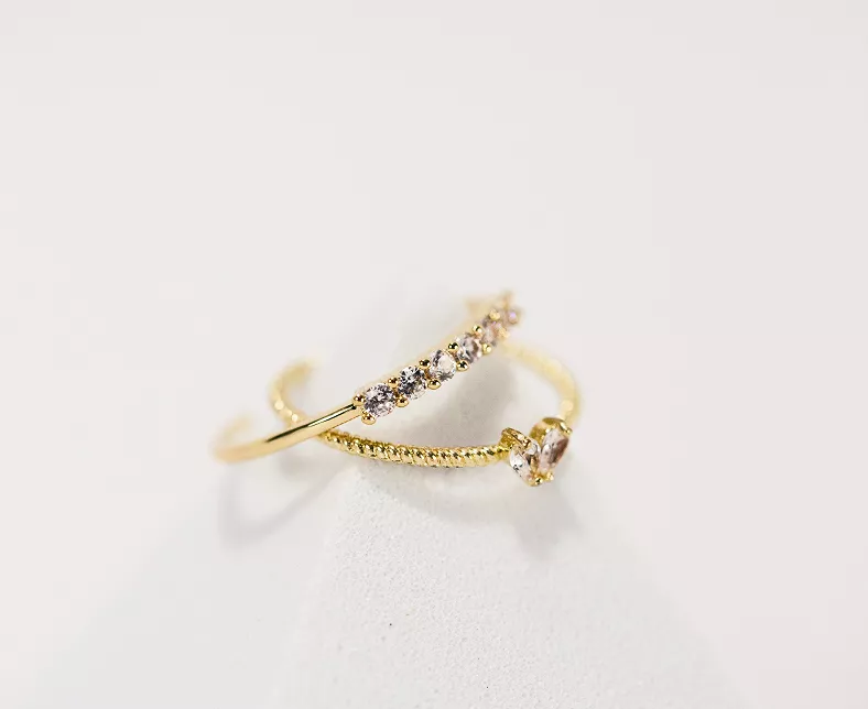 Two stacked gold rings with crystal accents - one bar design with row of stones, one with solitaire stone on white in delicate ring styling