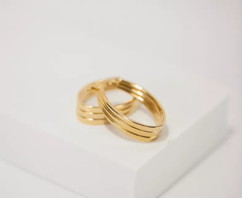 Polished gold triple-band stacked hoop earrings with modern ridged design resting on white angular surface in clean product photography
