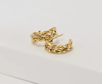 Polished gold triple-band stacked hoop earrings with modern ridged design resting on white angular surface in clean product photography