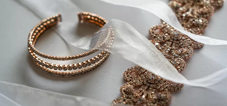 Rose gold jewelry collection with rhinestone bracelet and crystal earrings on white silk ribbon
