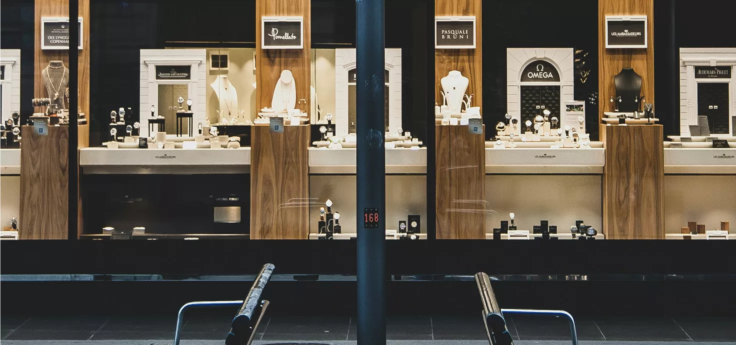 Jewelry store display windows with illuminated wooden showcases featuring luxury watches and accessories, viewed from outside mall