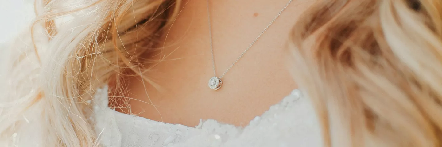 Blonde woman wearing a delicate silver necklace with a crystal pendant over a white lace-trimmed top