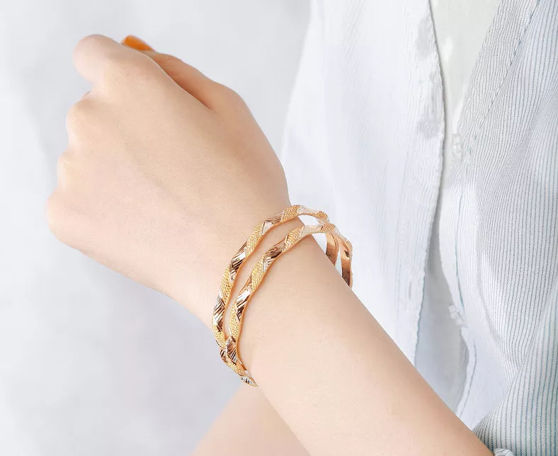 Gold twisted rope cuff bracelet worn on wrist with white ribbed long sleeve top, showing elegant braided metallic design and open-back style